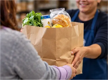 A volunteer handing over a bag of groceries.