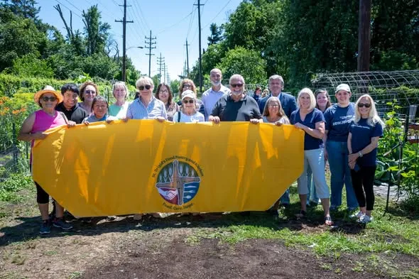 Volunteers and community partners holding the yellow St. Brigid's banner at the community garden ribbon cutting.